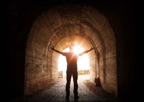 Person standing in dark tunnel looking toward the light symbolizing sexual assault recovery.