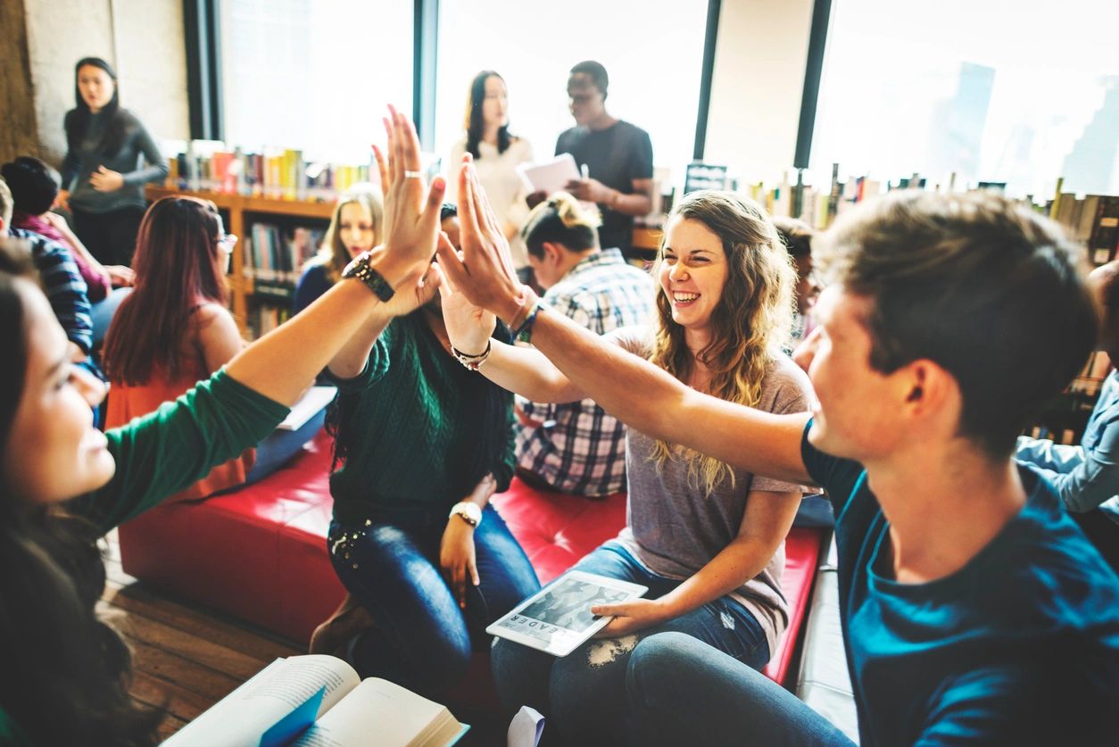Students sitting in a library doing a group high-five to celebrate disability rights and inclusion