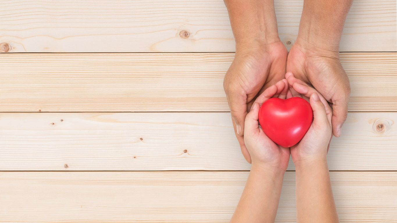 Two sets of hands rest in each other with the top hands holding a red heart. These hands remind the viewer to resolve to be kinder in 2026.