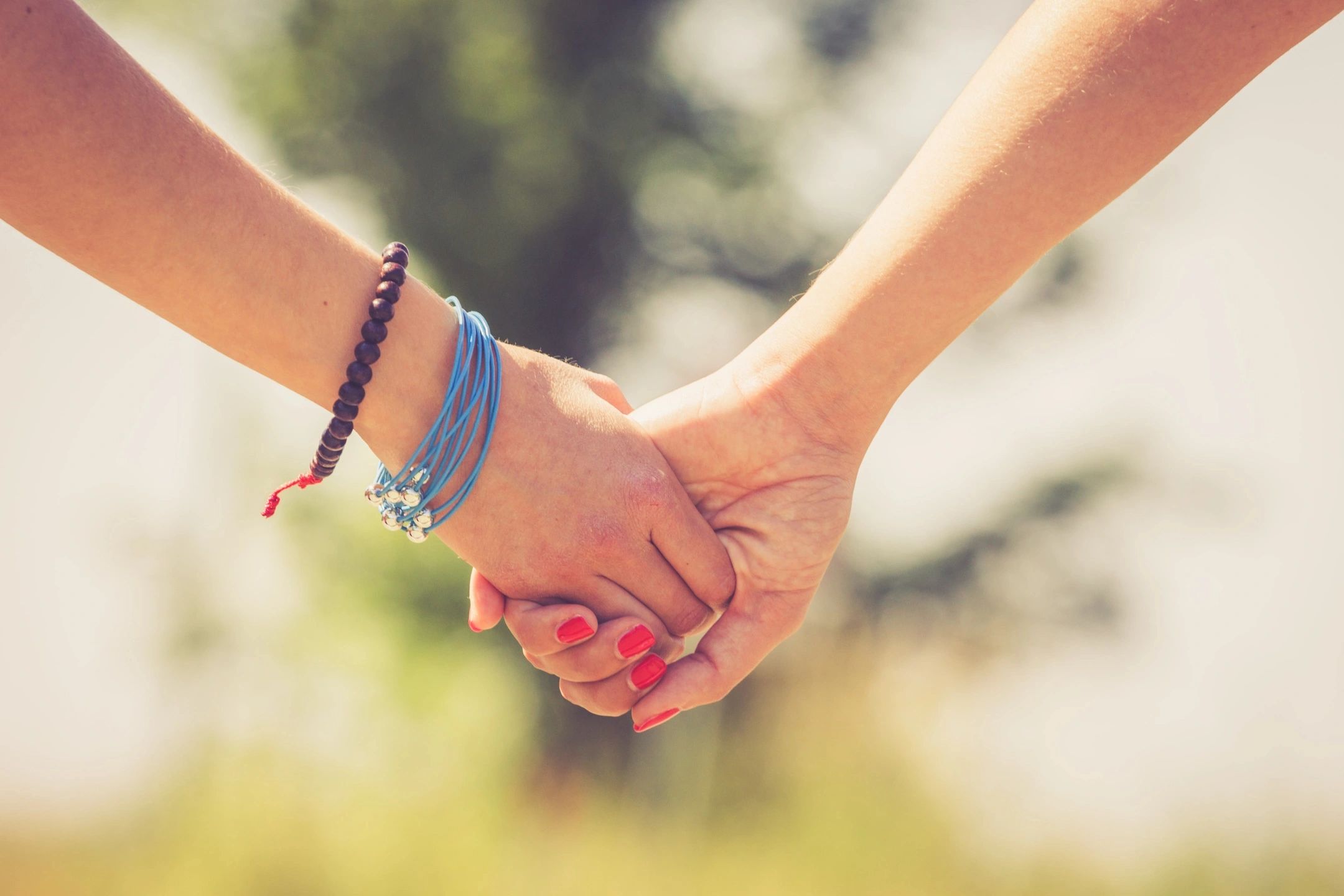Two arms are outstretched and holding hands. One arm has bracelets on it and the other shows polished fingernails. The image reminds the viewer that we can have different ideas of soulmates in our own way.