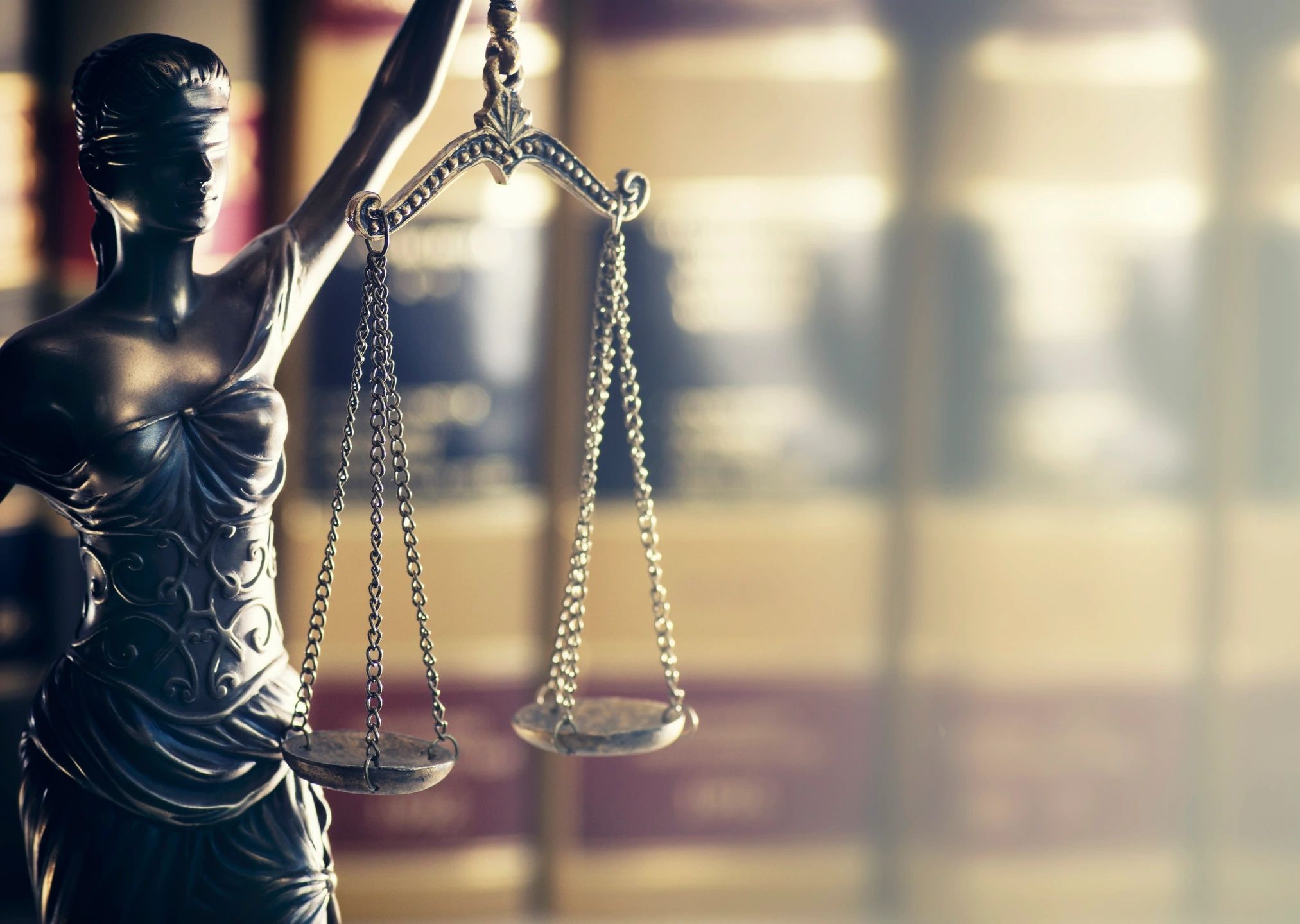 A statue of the scales of justice in front of law books. Disability advocacy works.